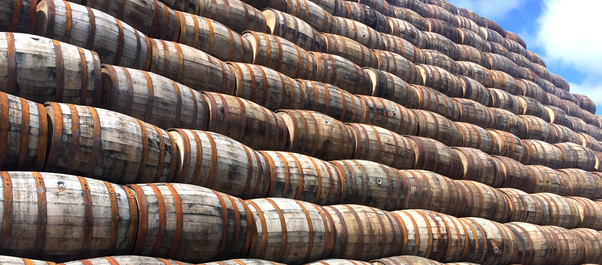 Een enorme stapel gerijpte whiskyvaten, keurig opgestapeld onder een heldere lucht. Deze visuele representatie van opslag toont het hart van waardeontwikkeling bij whisky: tijd, schaarste en vakmanschap – essentieel voor wie investeert in whisky.