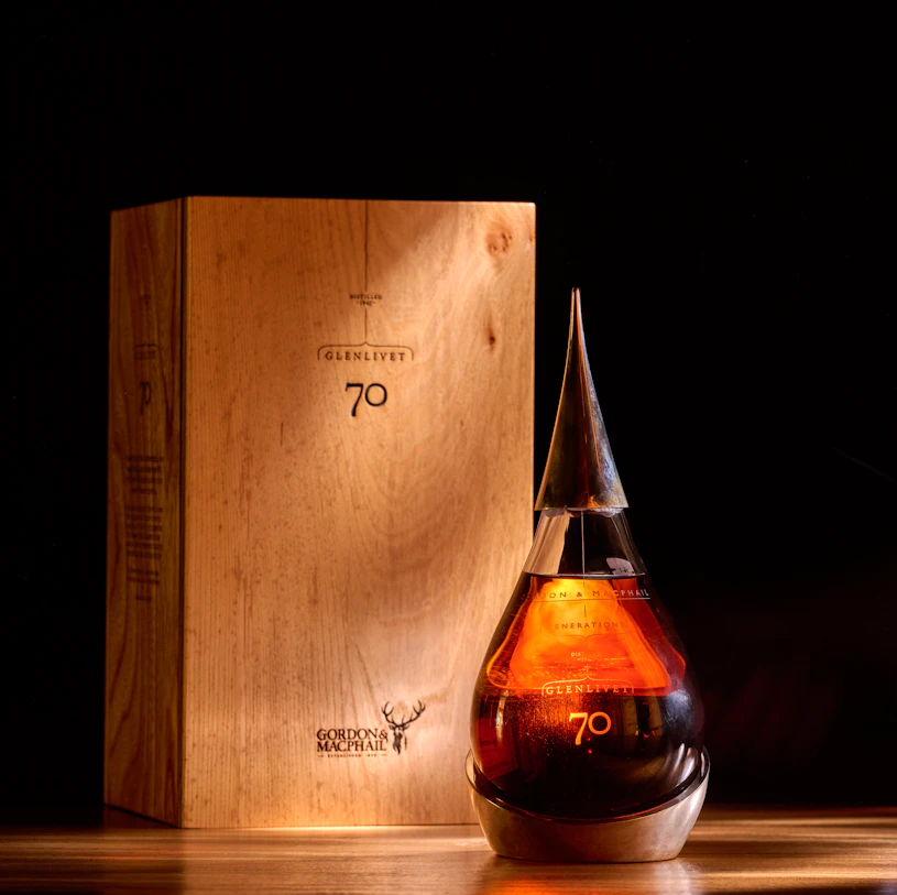 A rare bottle of Glenlivet 70 Year Old by Gordon & MacPhail, elegantly displayed beside a whisky glass in a warmly lit, luxurious setting. This extraordinary single malt captures craftsmanship, age, and value.