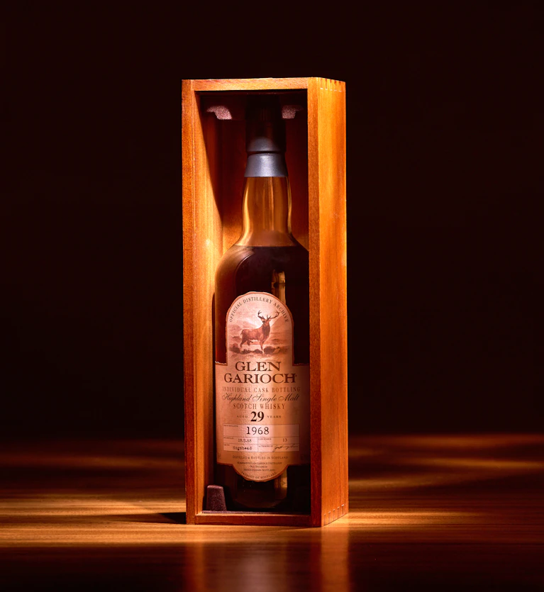 A bottle of Glen Garioch 29 Year Old single malt whisky (vintage 1968) stands upright in a wooden display case, warmly lit in a dark, elegant setting. This rare Highland whisky embodies heritage and is a valuable asset for long-term whisky investments.