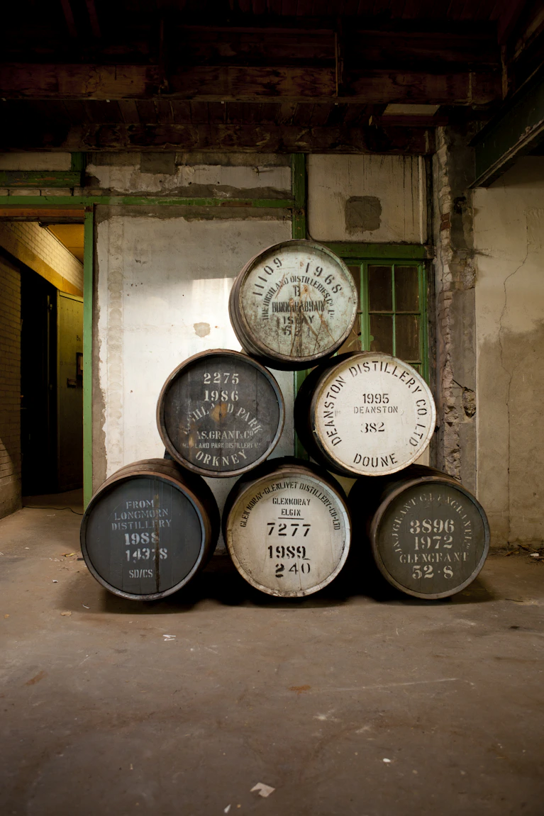 Zes authentieke whiskyvaten van Glen Grant, Deanston, Glen Moray, Longmorn, Highland Park en Bunnahabhain opgestapeld in een klassieke Schotse warehouse omgeving