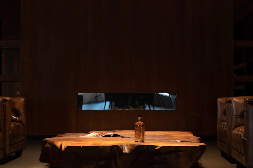 Luxe lounge in het hoofdkantoor van Scotch Whisky Investments in Sassenheim, voorzien van leren chesterfield fauteuils, een robuuste boomstamtafel met een fles zeldzame single malt whisky en een warme, exclusieve sfeer voor klantgesprekken.