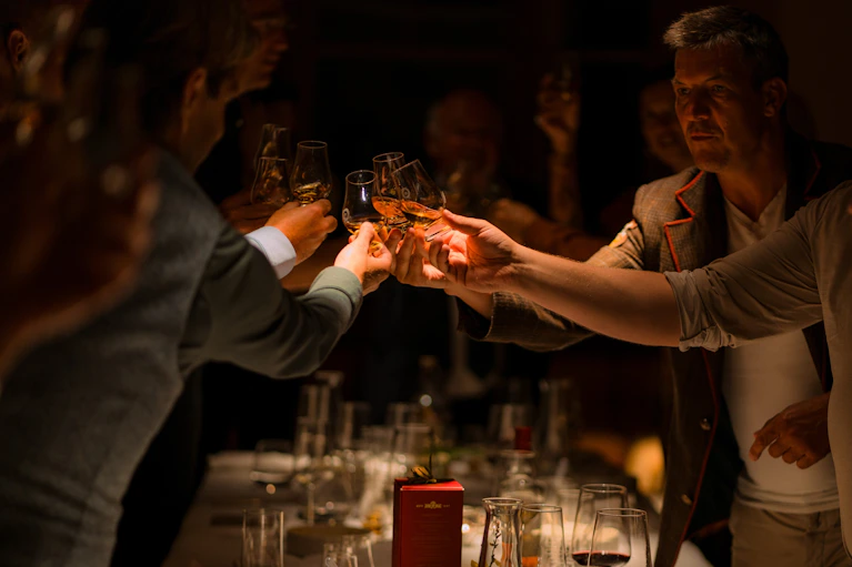 Group of Scotch whisky investors raising their glasses in a toast during an exclusive evening event and tasting dinner in Scotland