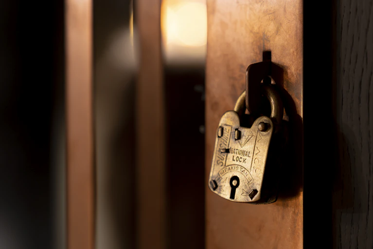 Close-up van een vintage messing hangslot dat de koperen toegangspoort van de exclusieve whiskyruimte The Unprecedented beveiligt.