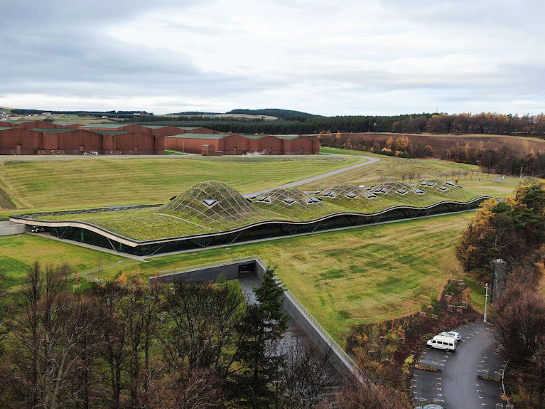 Wide aerial view of the modern Macallan distillery building with its signature undulating green roof on the Easter Elchies estate in Speyside.