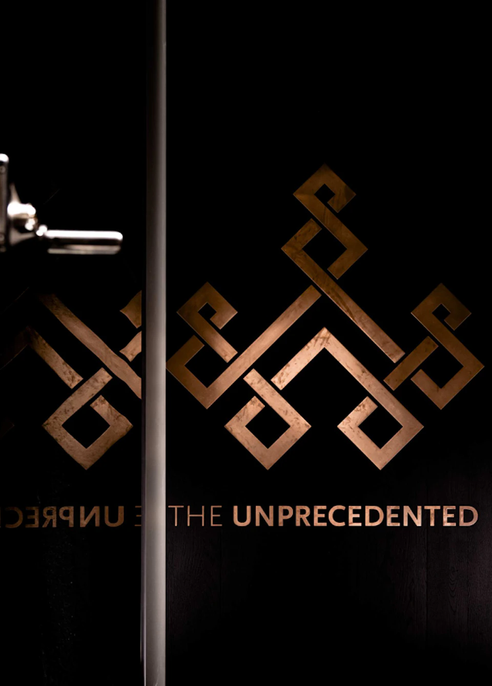 Koperen logo op een donkere deur met de tekst The Unprecedented