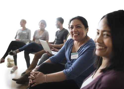 6 adults sitting in a line looking towards each other smiling