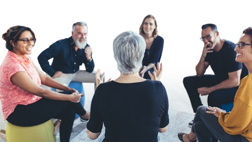 6 adults sit in a circle smiling and having a discussion