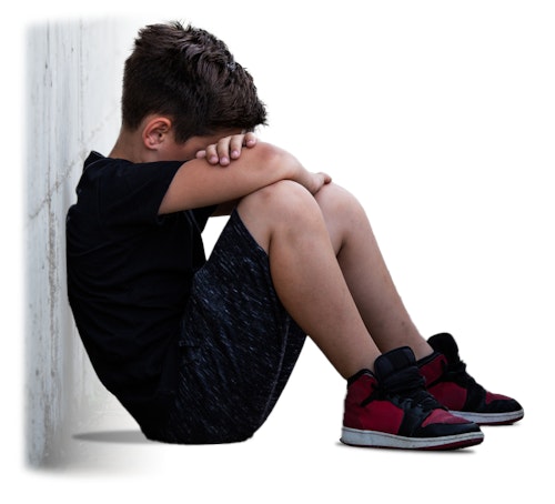 Young boy sitting down leaning against the wall. His hands are crossed and his head place in his arms