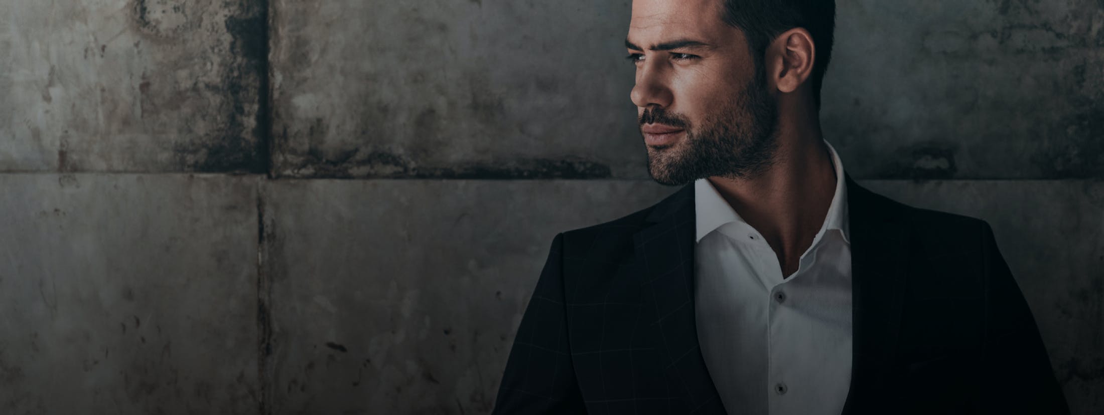 man in a suit and white shirt standing in front of a wall