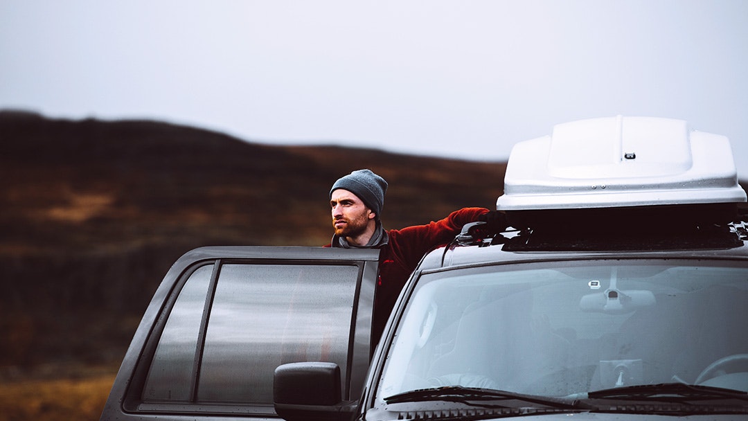 Man standing next to a car with roof rack and box in nature