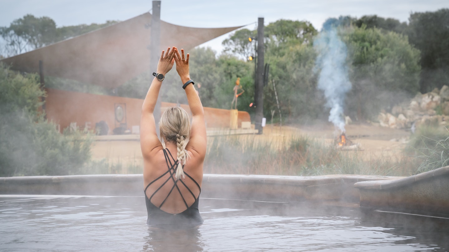woman with arms up during hot springs yoga in the pool with steam