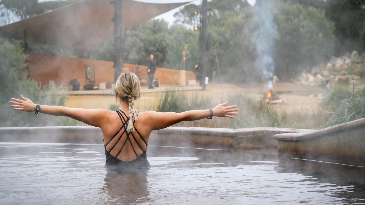 woman with arms out during hot springs yoga in the pool with steam