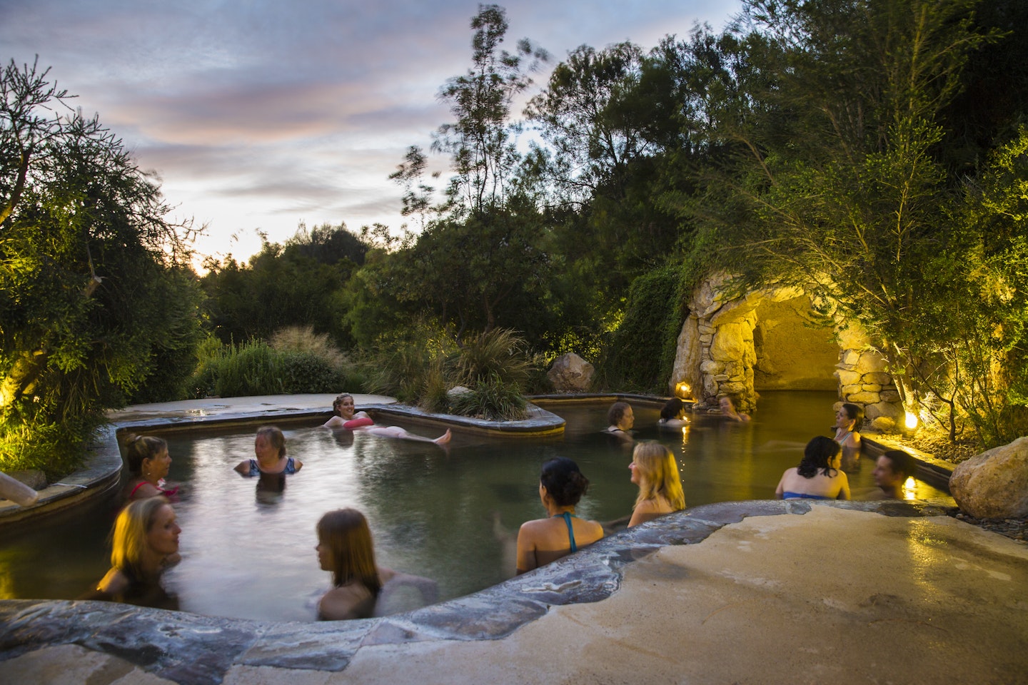women bathing in geothermal pool with a cave in the background and garden lights