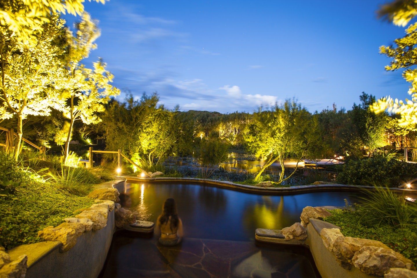 girl sitting on the edge of lakeside pool at twilight, staring at a blue sky