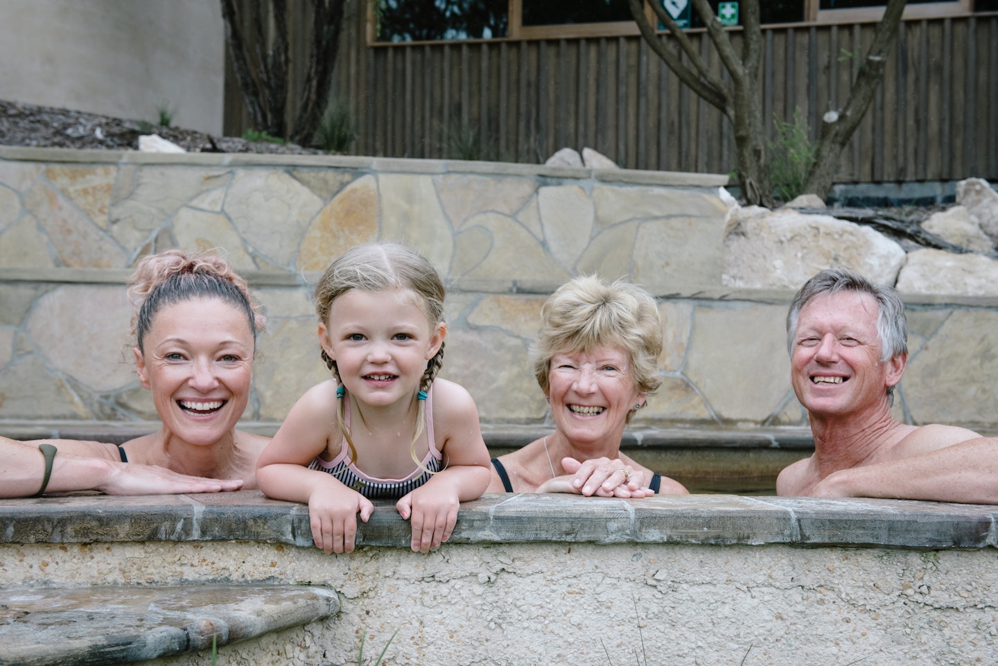 group of adults and one girl child looking at camera smiling while bathing in hot spring