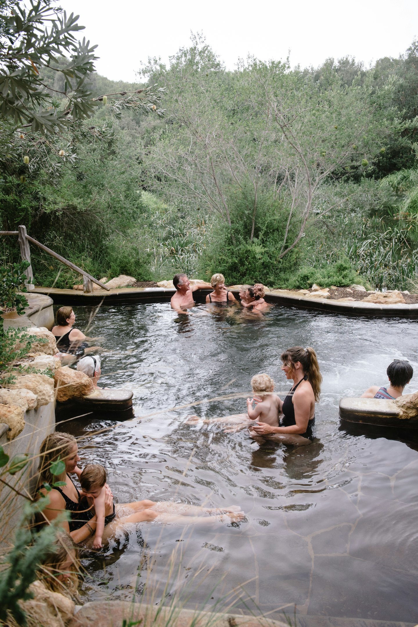 group of adults and children bathing in hot pool overlooking greenery