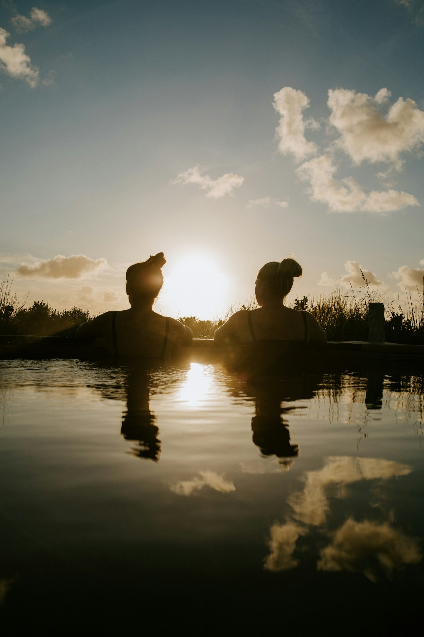 the back of two women as they look out at the sunset while bathing in geothermal pool