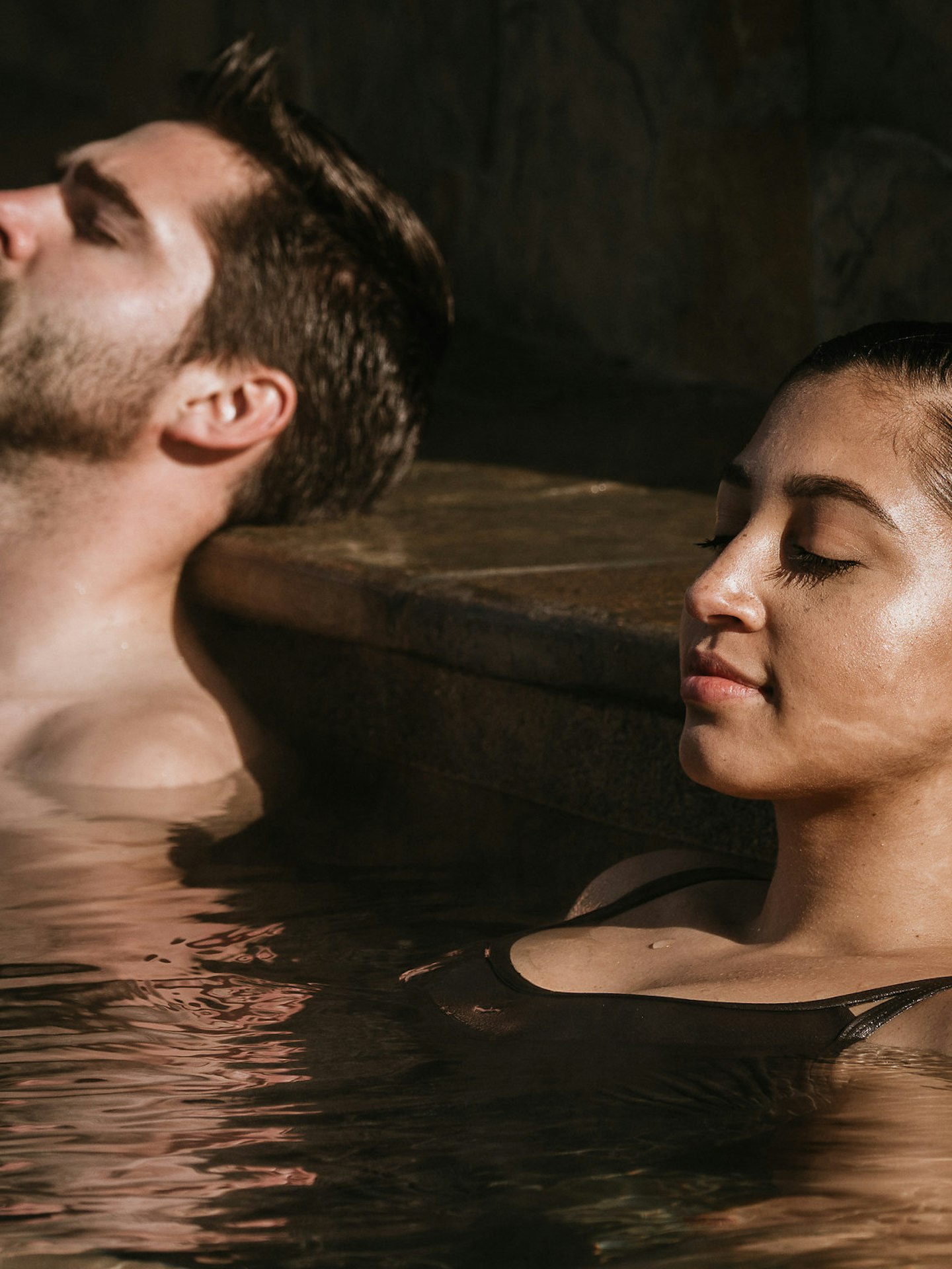 man and woman with eyes closed soaking in geothermal pool