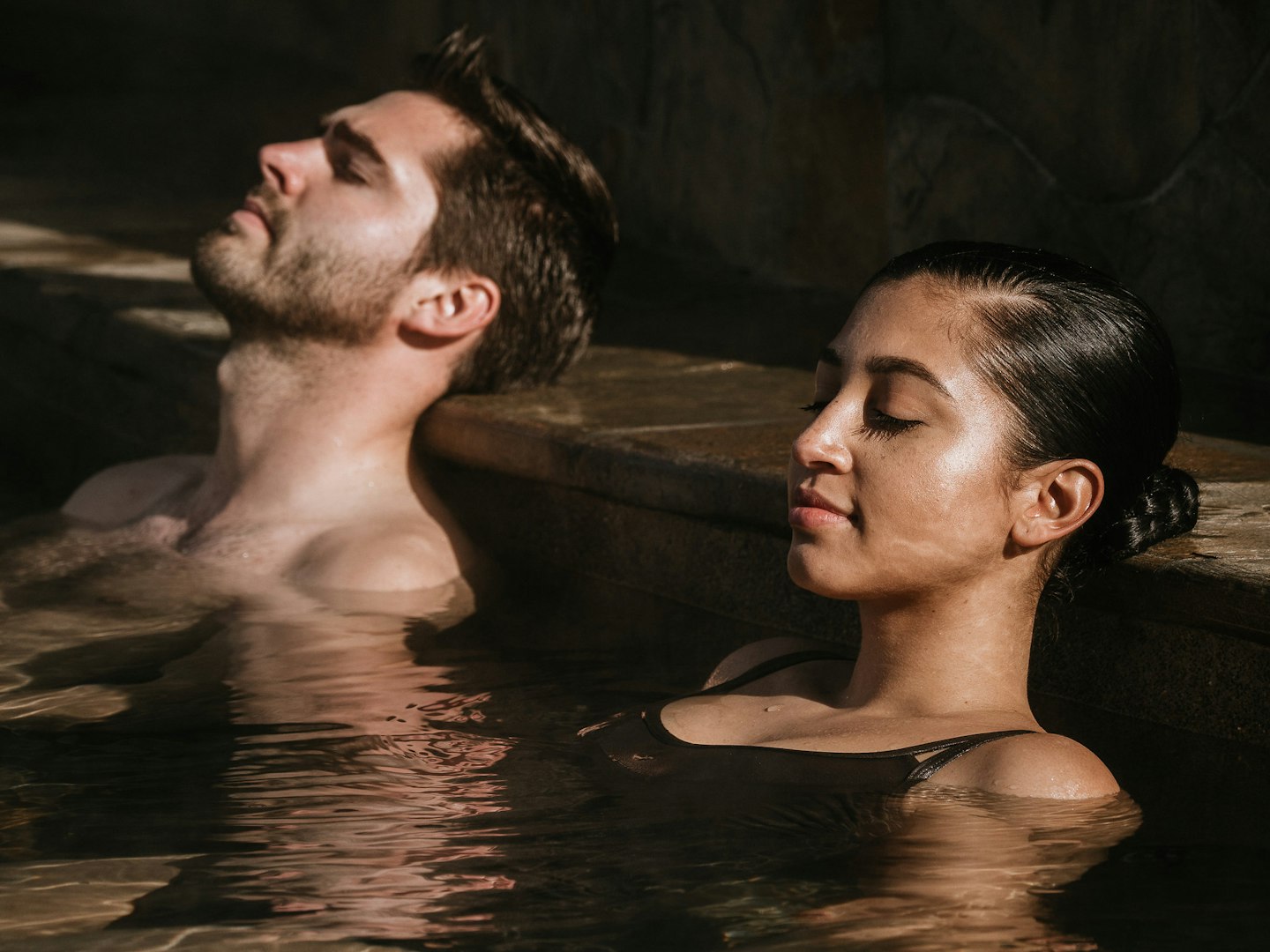 man and woman with eyes closed soaking in geothermal pool