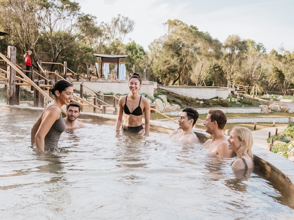 three men and three women smiling while sitting and standing in amphitheatre hot pool