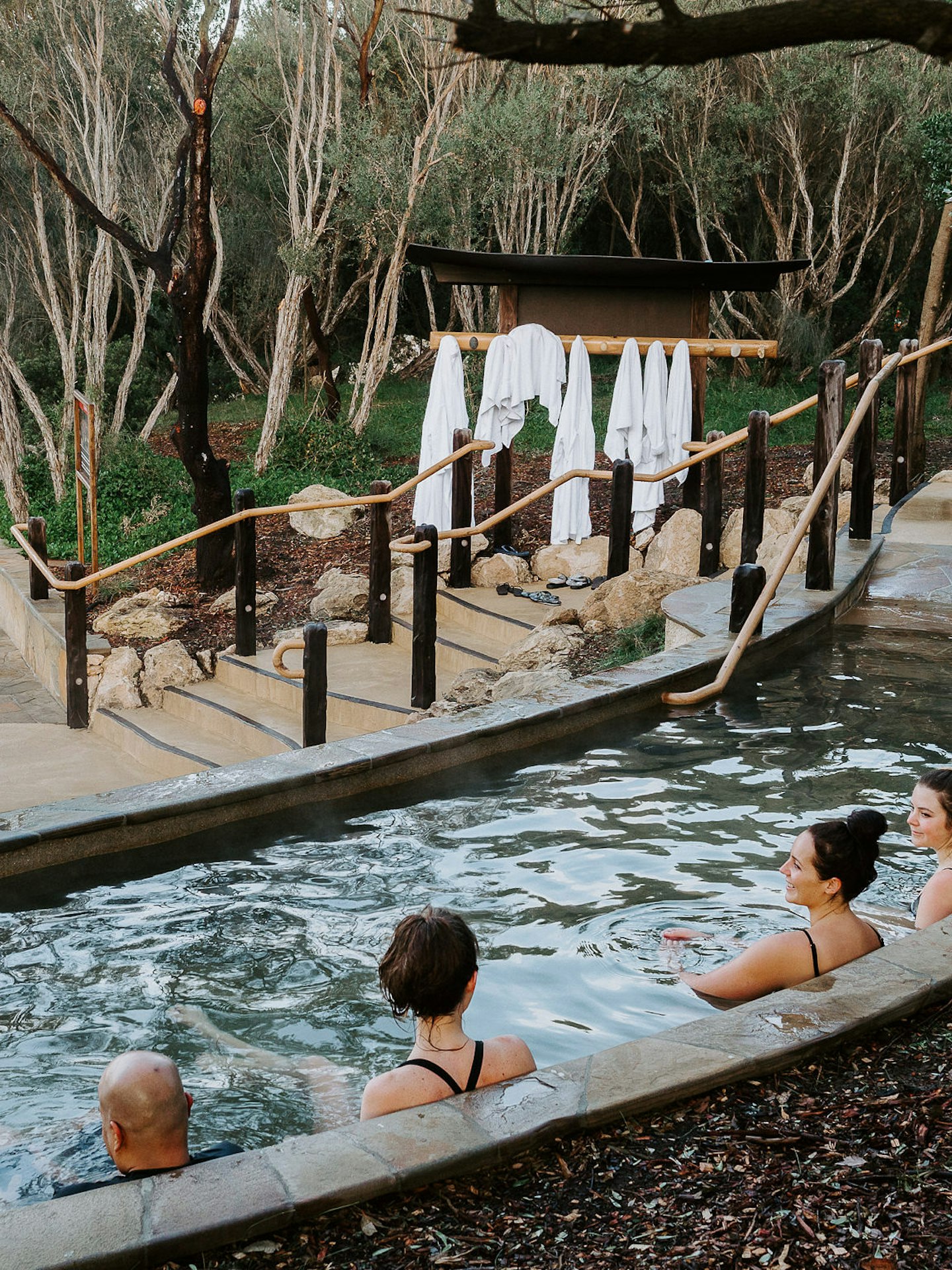 group of friends sitting in amphitheatre pool with trees and hanging bath robes in background