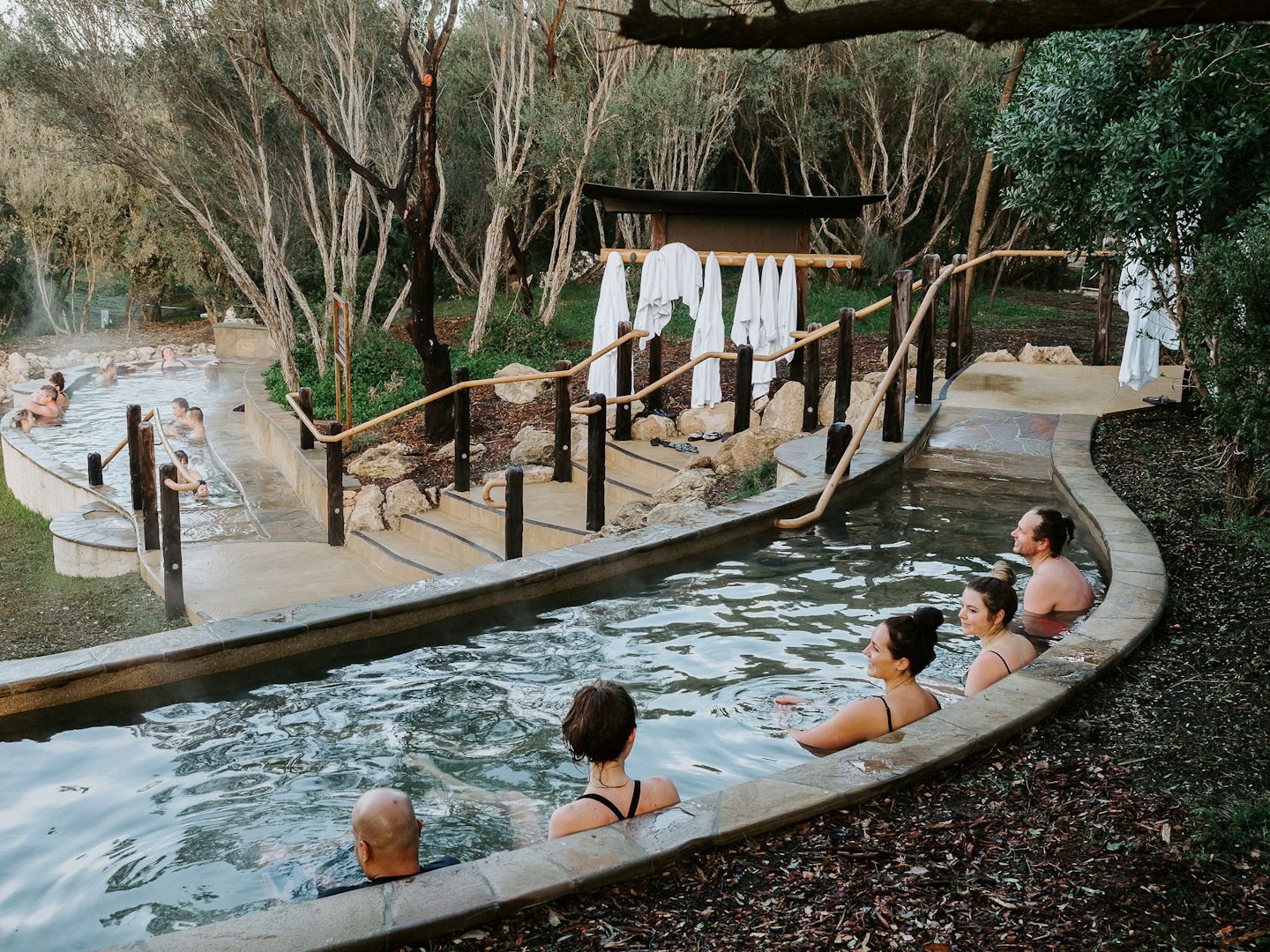 group of friends sitting in amphitheatre pool with trees and hanging bath robes in background