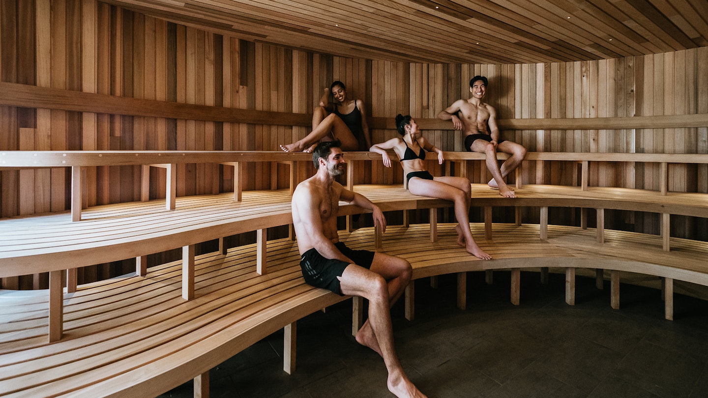 four people in bathing suits sitting in large wooden sauna