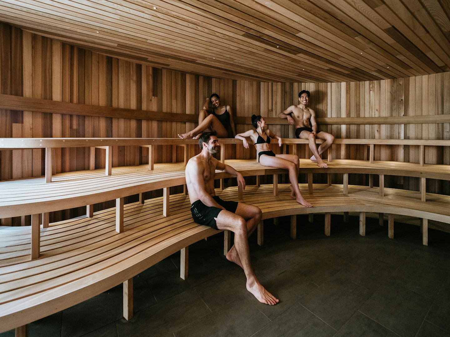 four people in bathing suits sitting in large wooden sauna