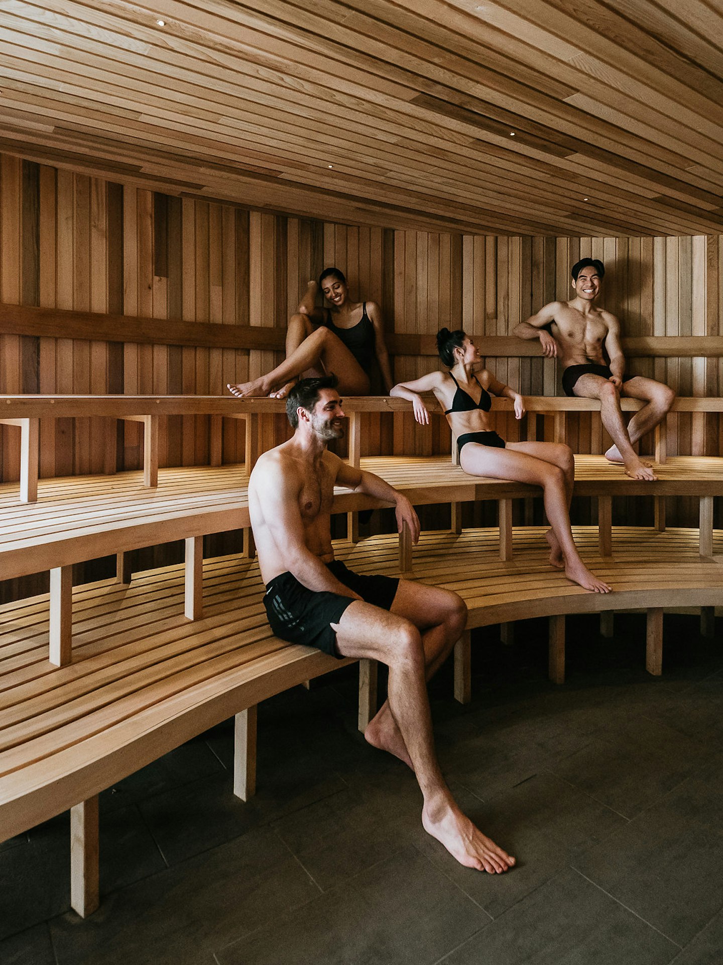 four people in bathing suits sitting in large wooden sauna