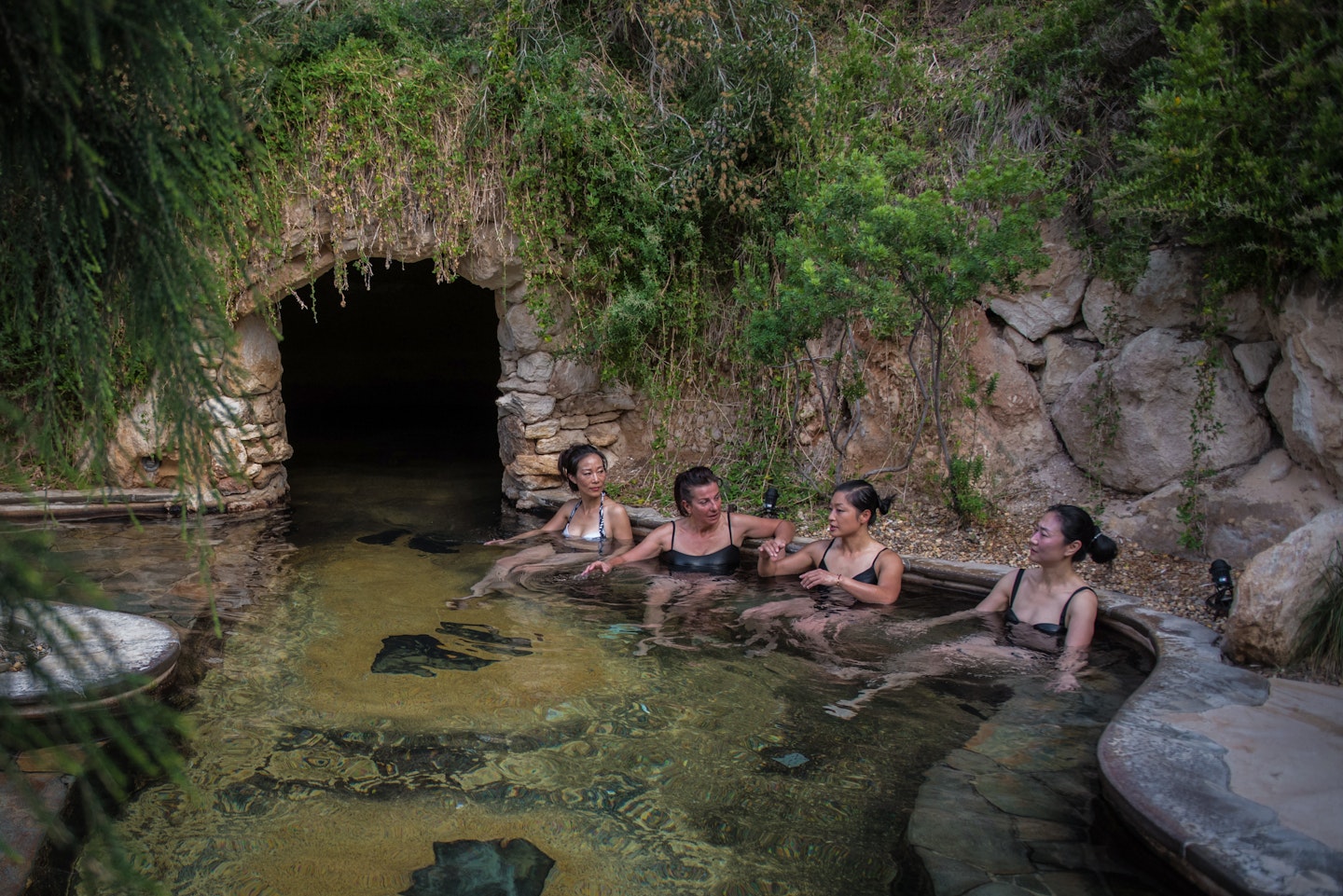 group of ladies sitting in geothermal waters outside entrance to cave pool