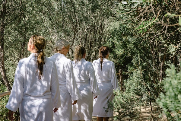 four women in white bath robes walking through nature