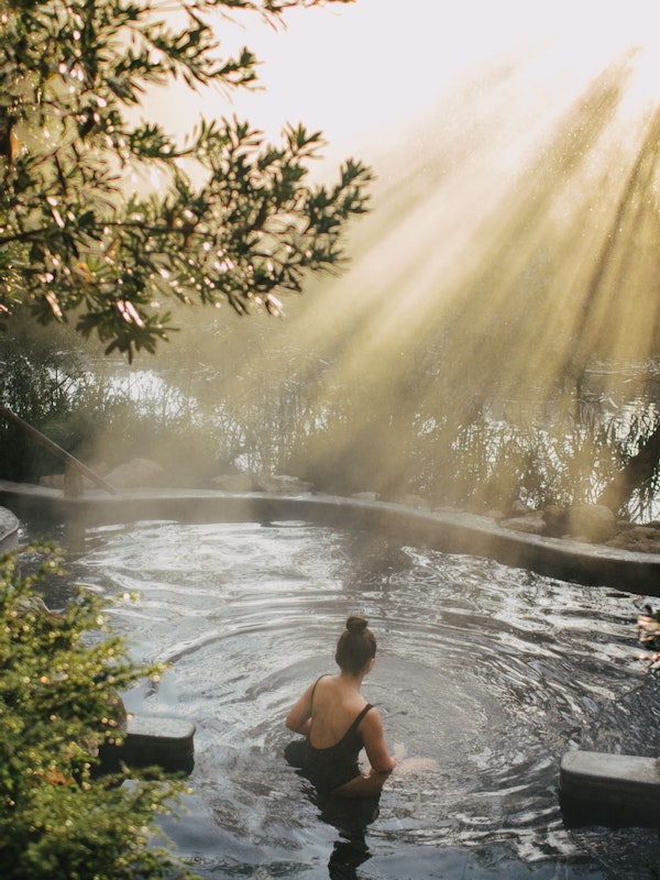 girl in black bathing suit sitting in hydrotherapy pool with sunlight breaking through trees