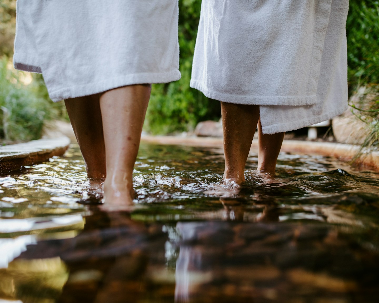 two people in white bath robes visible from knee down, walking in geothermal waters on reflexology walk