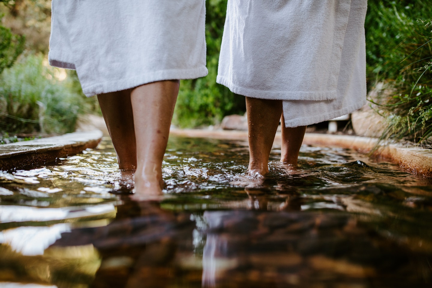 two people in white bath robes visible from knee down, walking in geothermal waters on reflexology walk