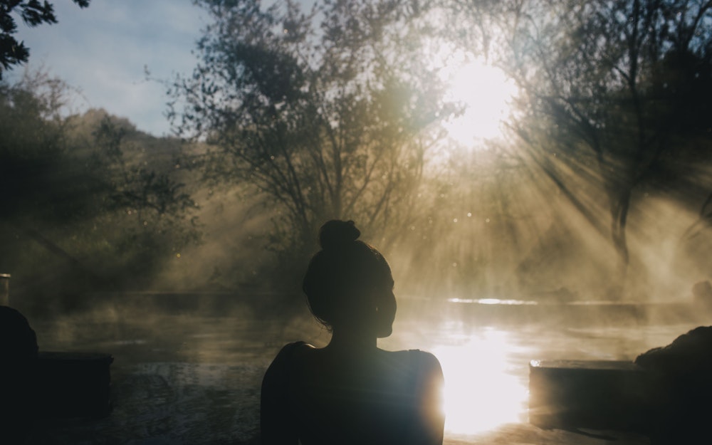 woman sitting in steamy hot pool with sun breaking through the trees