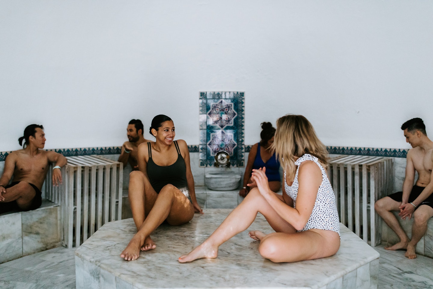 men and women in bathing suits sitting in marble turkish steam room