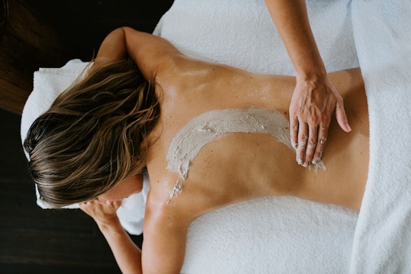 Woman lying face down on treatment table receiving a clay massage