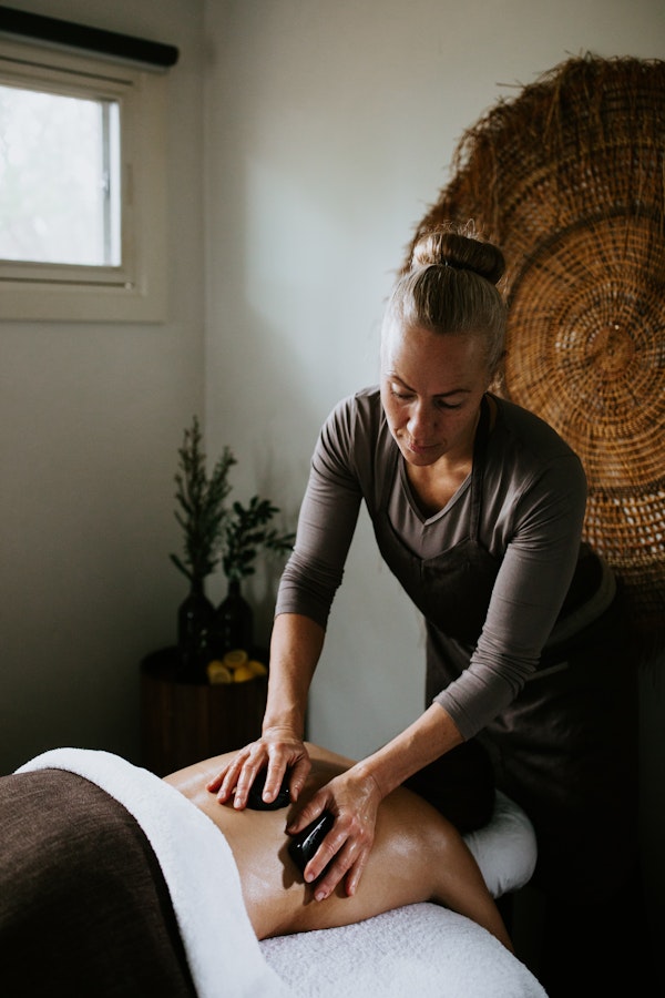 lady lying facedown on treatment table with therapist conducting hot stone massage on her back