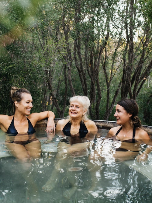 three ladies in black bathing suits sitting in barrel pool with nature all around