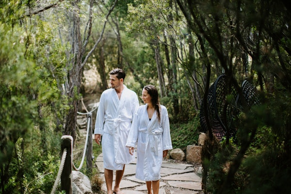 man and woman in white bath robes walking along path in nature surrounded by trees