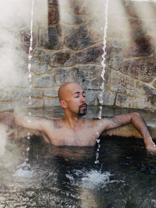 man sitting in geothermal pool with three streams of water falling around him