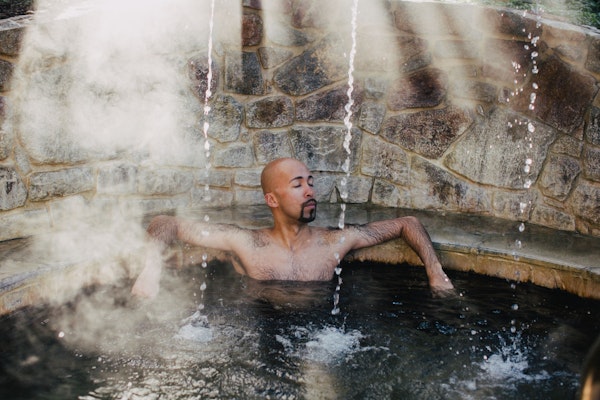 man sitting in geothermal pool with three streams of water falling around him