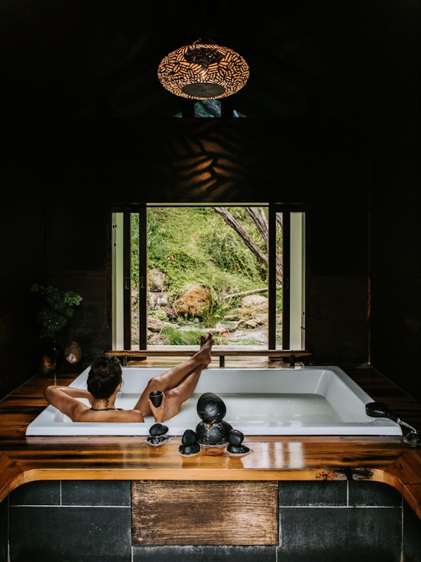 woman relaxing in private bathing pavilion with legs crossed on bath edge, looking out at nature's view