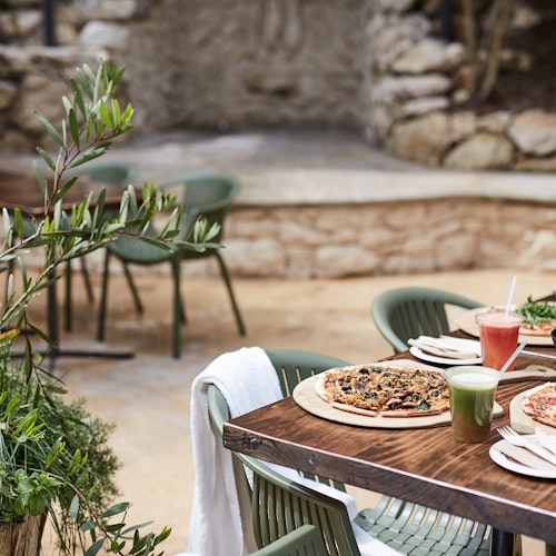outdoor café table with pizzas, fresh juices and a salad laid out