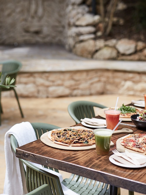 outdoor café table with pizzas, fresh juices and a salad laid out