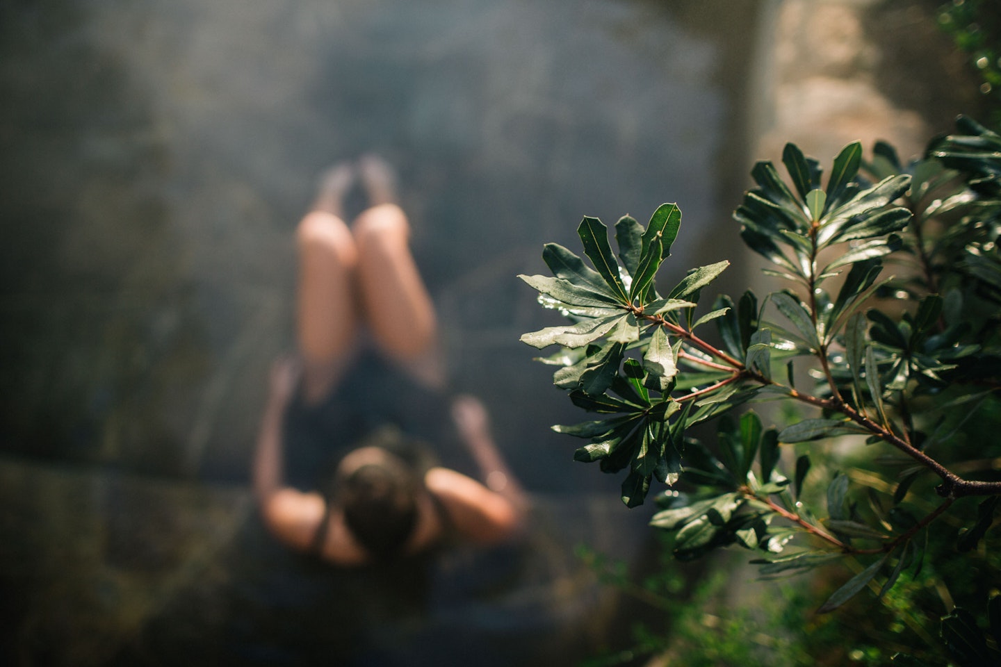 bird's eye view of lady in bathing suit sitting in geothermal pool with foliage in foreground