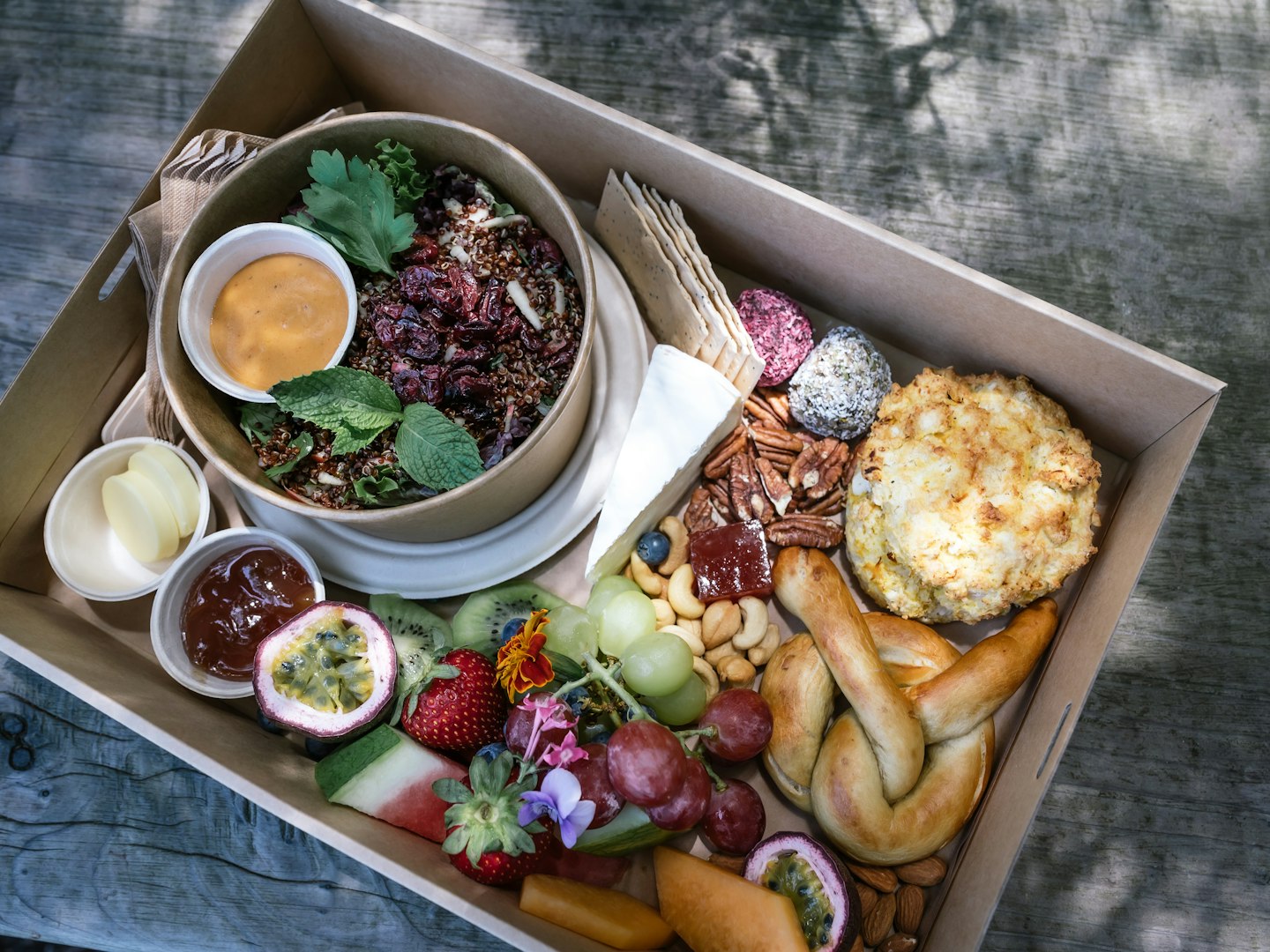 picnic hamper in cardboard box with salad, pastries, fruit, cheese and condiments