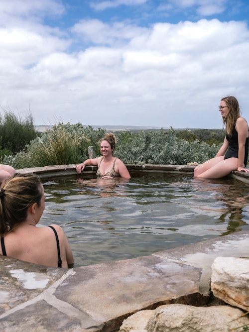 women sitting in and around hilltop geothermal pool with 360 degree view