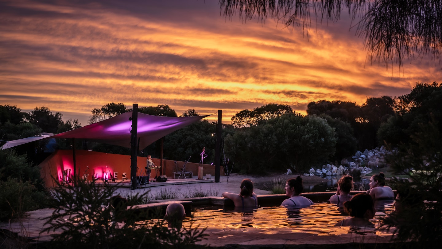 people sitting in geothermal pools at sunset looking out to performance on amphitheatre stage