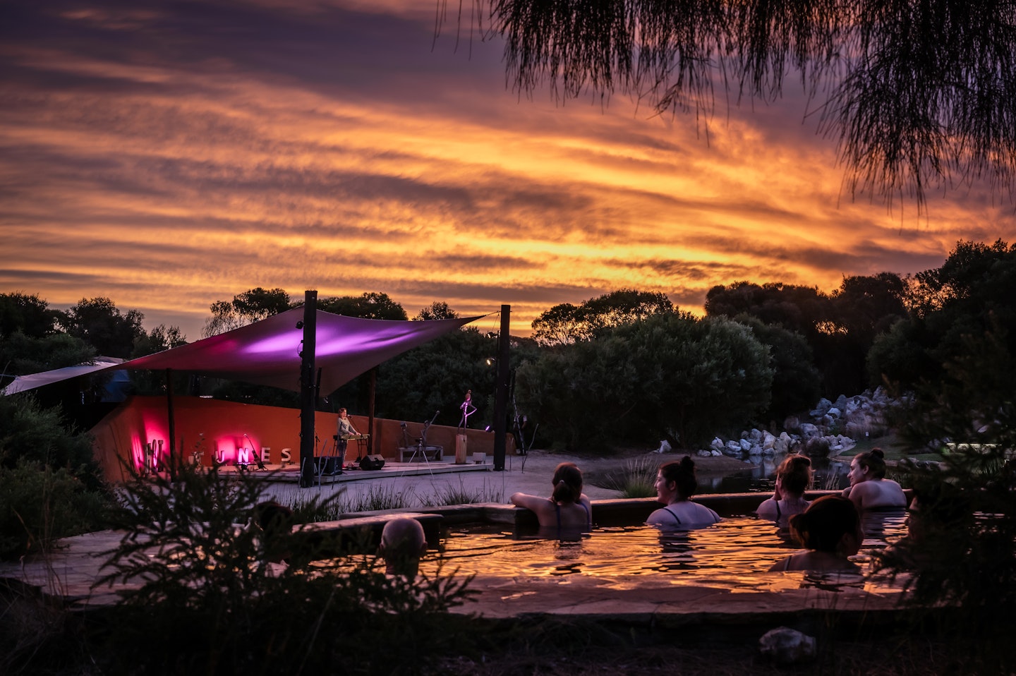 people sitting in geothermal pools at sunset looking out to performance on amphitheatre stage